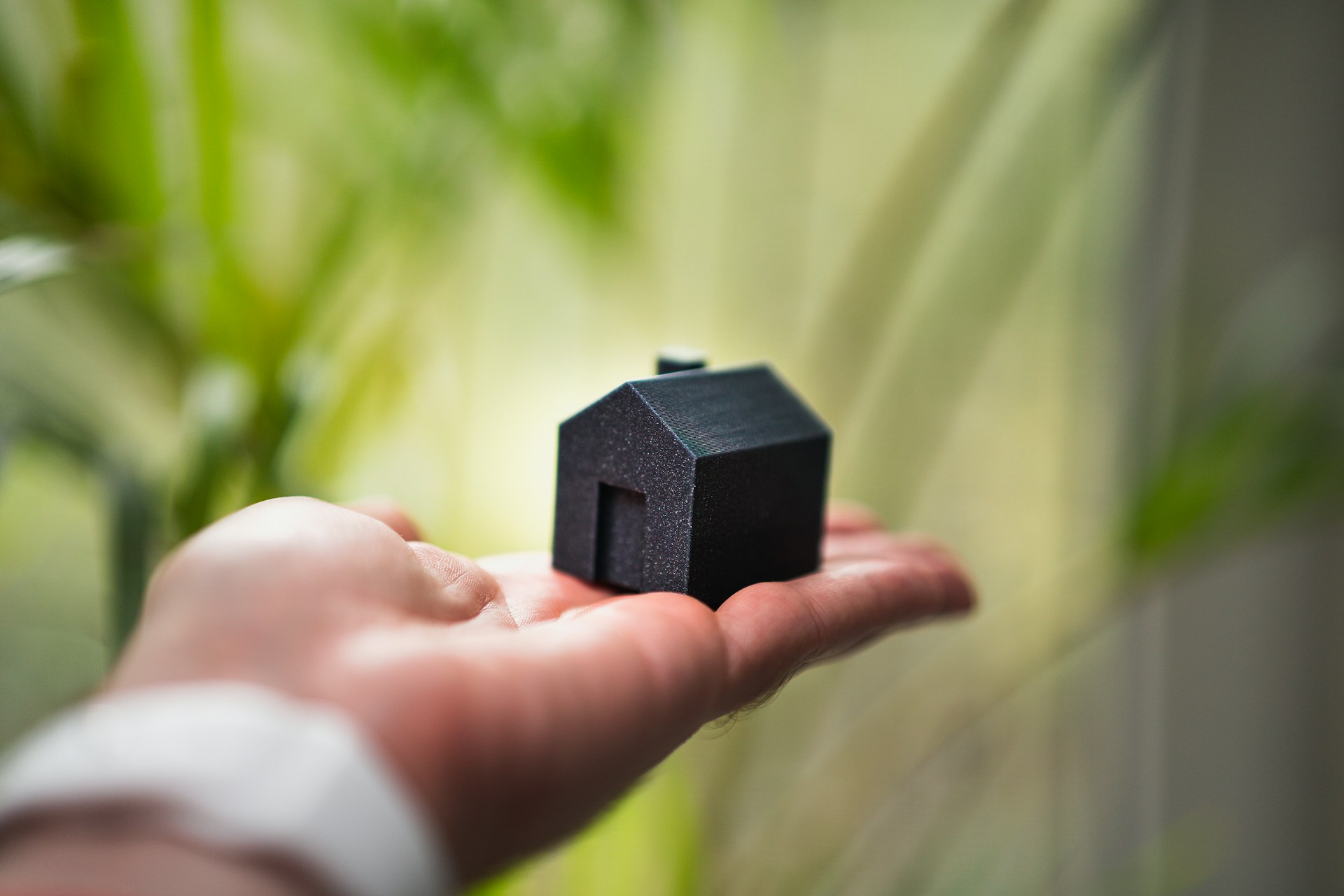 kleines schwarzes Modellhaus auf Hand als Symbol für unnötige Versicherungskosten